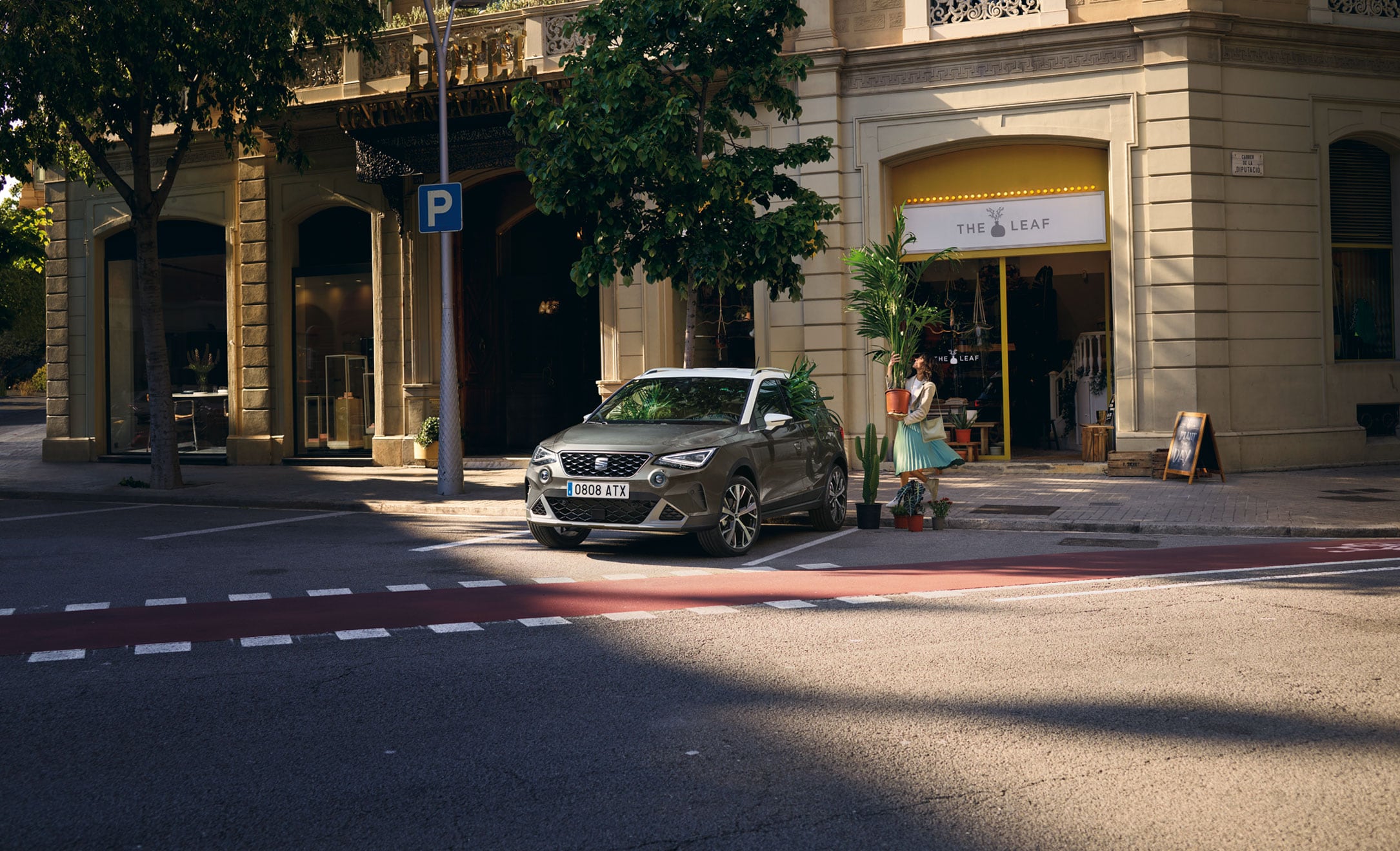 Vrouw loopt naar een SEAT Arona in Dark Camouflage met dak in Candy White om er een plant in te zetten