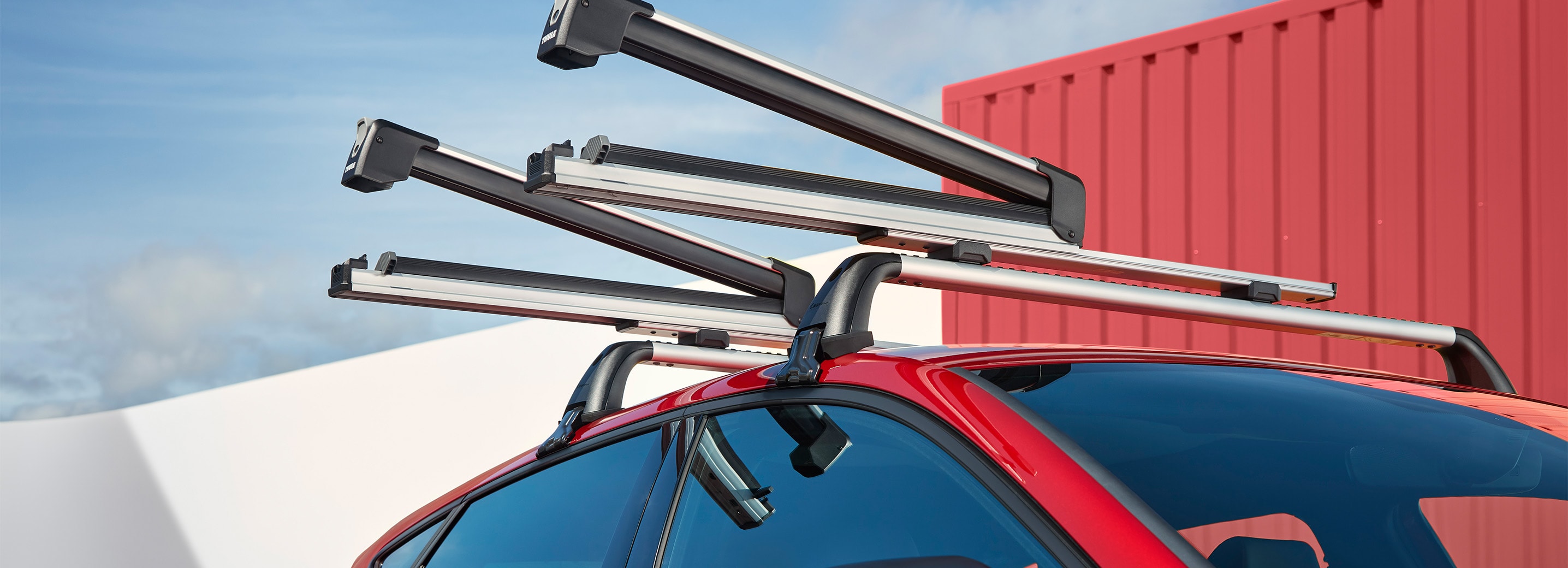 Une seat leon rouge garée à l’extérieur, mettant en valeur les barres de toit accueillant plusieurs paires de skis.