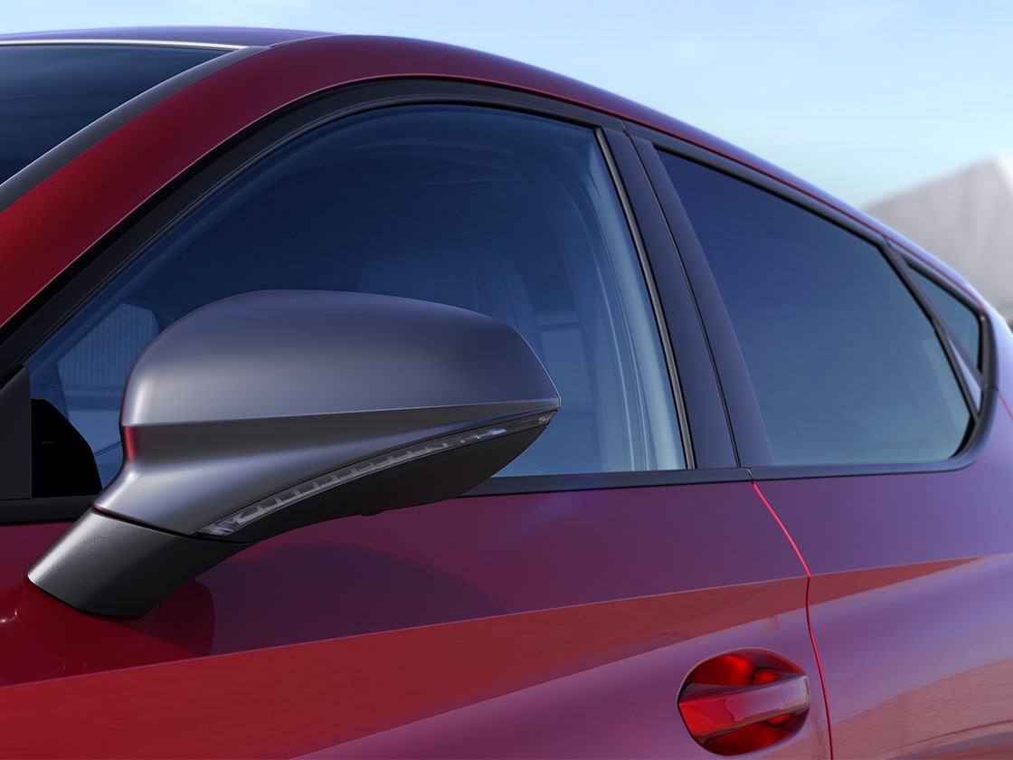 Vue latérale d’une SEAT Leon 5D rouge garée dans un environnement extérieur ensoleillé mettant en valeur les détails extérieurs du pack FR.
