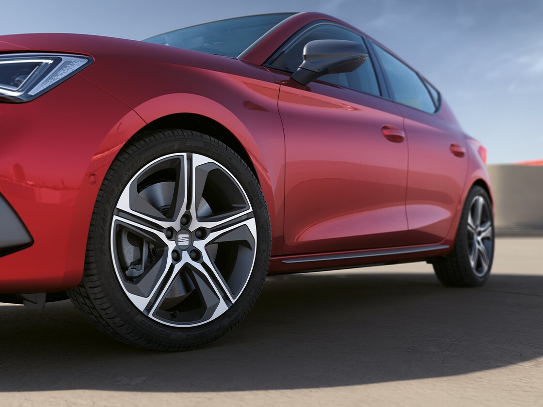 Une seat leon rouge désir mettant en valeur la moulure de portière et les jantes en alliage, garée sous un ciel totalement dégagé.