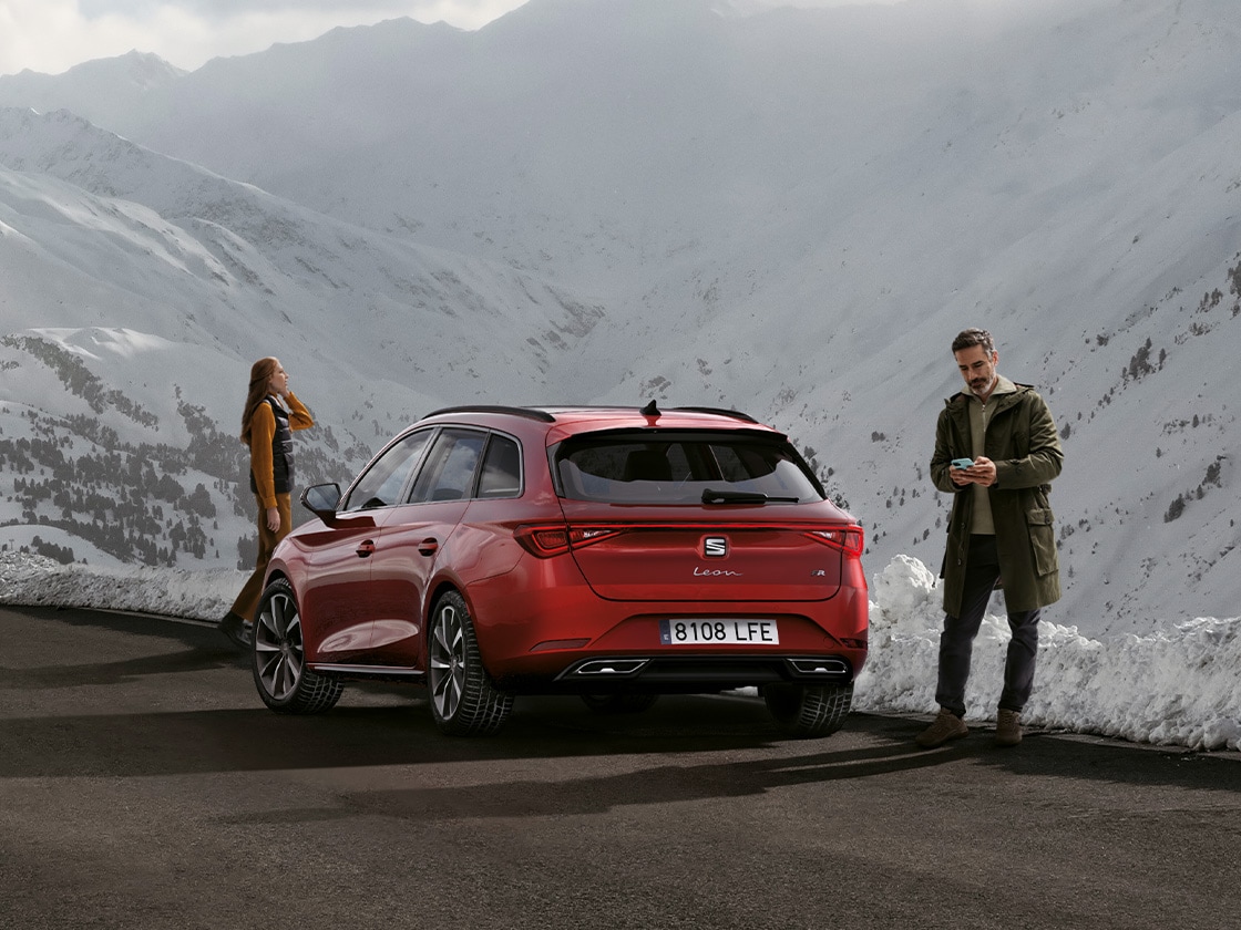Image ALT: Une seat leon rouge garée sur une route de montagne, attendant de bénéficier des avantages de mobilité et de l’assistance routière seat service. Deux personnes se tiennent à proximité.