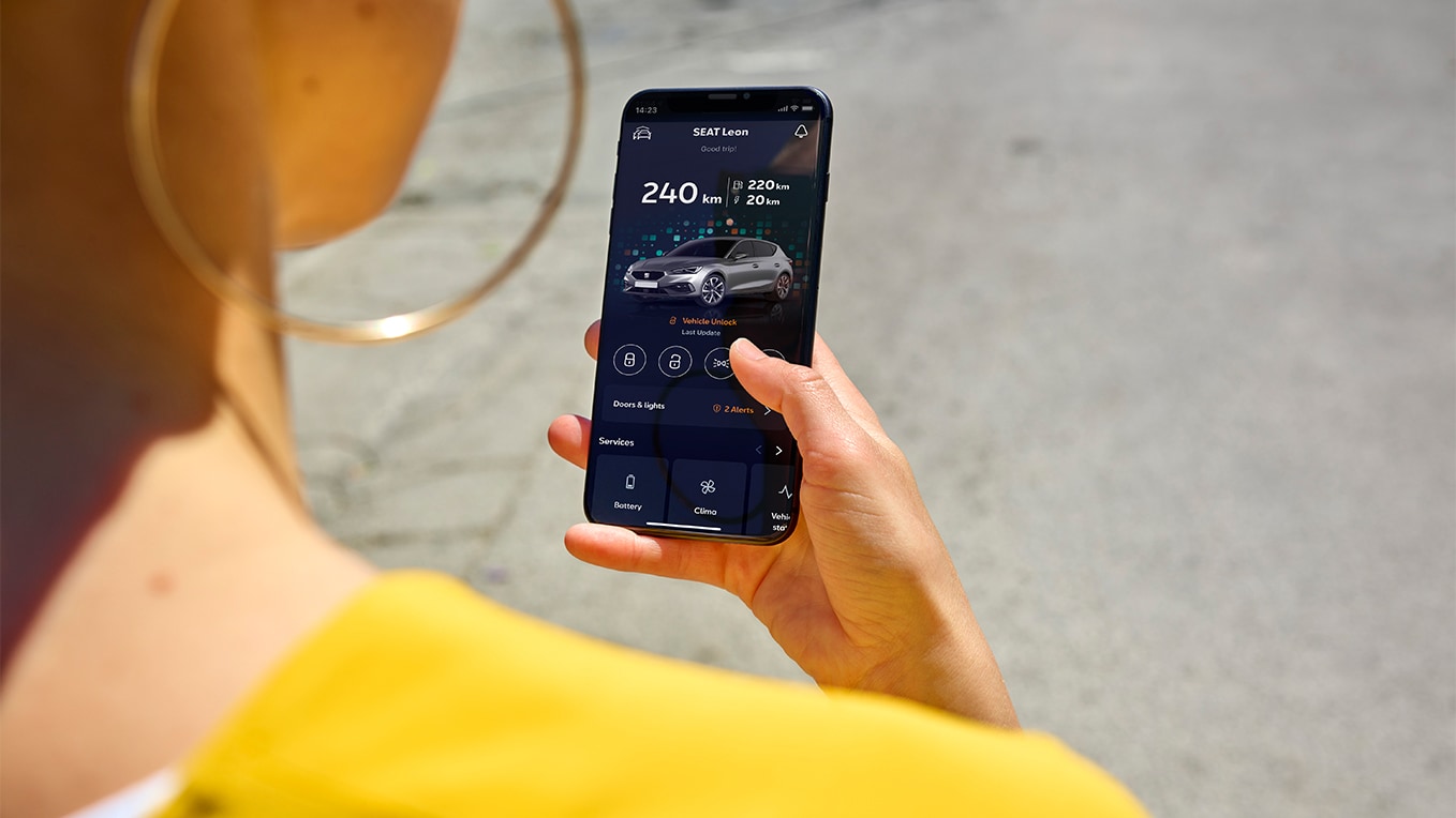 Une personne tenant un smartphone utilisant l’application my seat, une fonctionnalité de seat connect, pour accéder à distance aux fonctionnalités du véhicule.