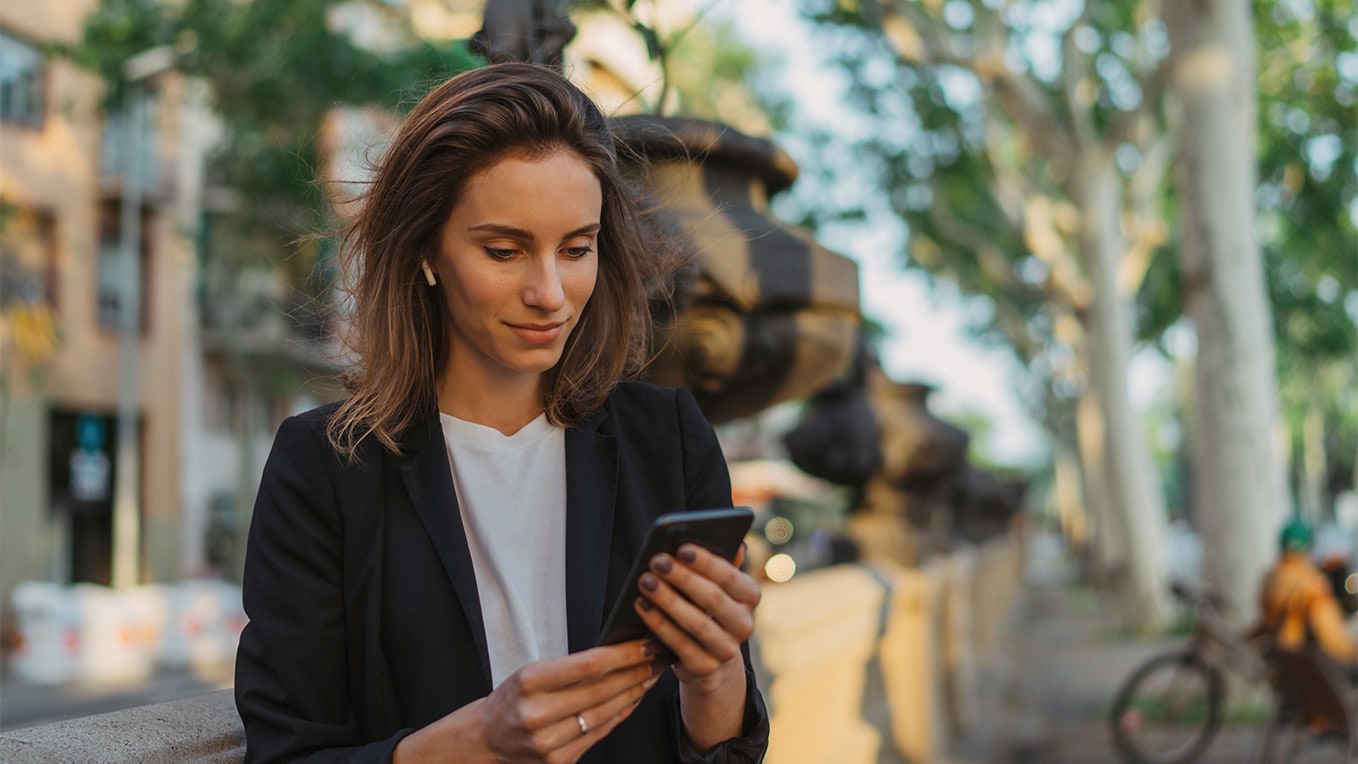 Femme utilisant son téléphone portable pour se connecter à seat connect, debout contre un mur en béton au milieu de la ville.