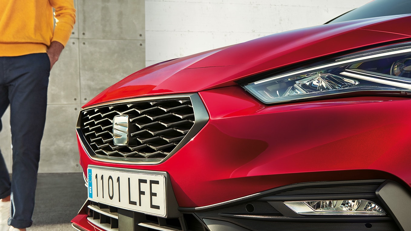 Gros plan sur la calandre de la seat leon en rouge désir, mettant en valeur son motif en nid d’abeilles fougueux et raffiné.