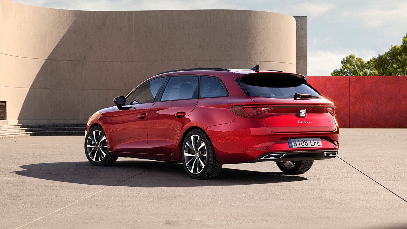 Vue de 3/4 arrière du break seat, la seat leon break en rouge désir, garée face au mur d’un bâtiment en extérieur. La vue met en valeur le design arrière de la voiture.